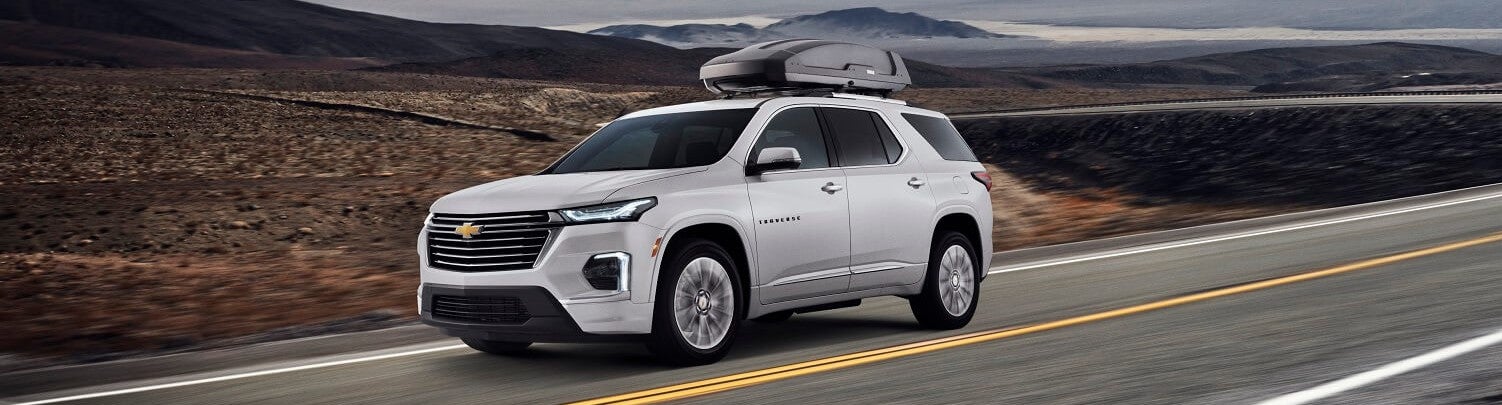 white silver chevy traverse driving fast with a cartop carrier on a remote desert road