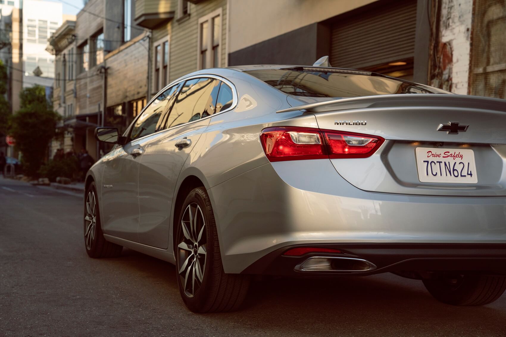 silver chevy sedan driving down narrow city street